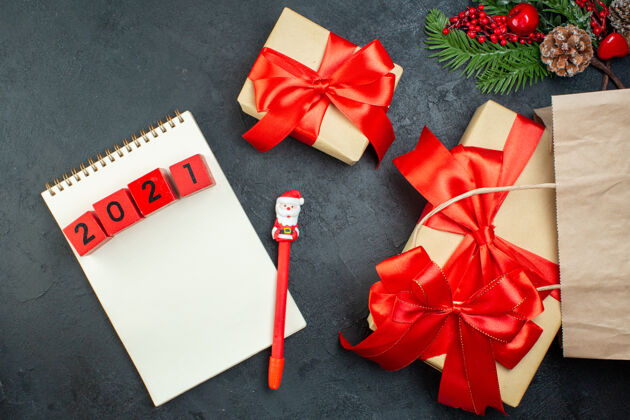 轮子上图是圣诞节的气氛与美丽的礼物与红色丝带和笔记本上的数字与笔在黑暗的背景圣诞节蝴蝶结笔记本