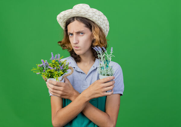 穿年轻的园丁 穿着连体衣 戴着帽子 手里拿着盆栽植物男人皱眉帽子