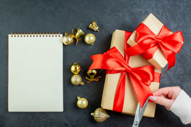 螺旋上图为黑色背景上螺旋笔记本旁边的礼品盒和装饰配件上手工切割的红丝带圣诞节蝴蝶结轮子