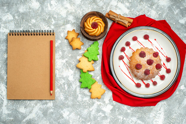 盘子俯视图白色椭圆形盘子上的浆果蛋糕红色披肩笔记本红色铅笔饼干灰色表面浪漫笔记本披肩