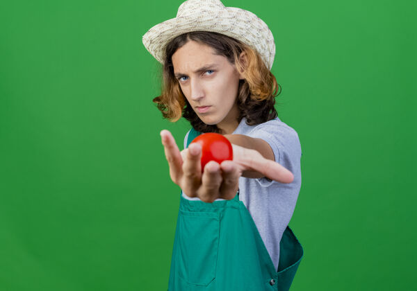 穿年轻的园丁 穿着连体衣 戴着帽子 脸上露出一脸严肃的新鲜西红柿脸站连身衣