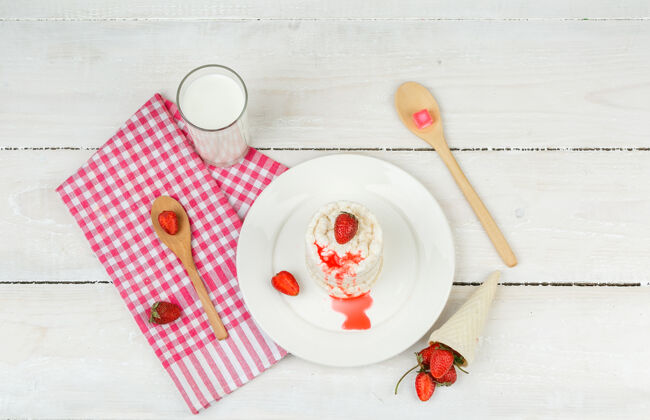 木头顶视图：白色米片放在盘子里 红色方格桌布 草莓 木勺和牛奶放在白色木板上水平脆饮食奶酪