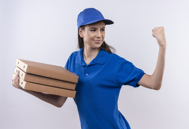 帽子身穿蓝色制服 头戴鸭舌帽的年轻送货女孩手持一叠披萨盒 自信地握紧拳头 赢家概念盒子握紧拳头