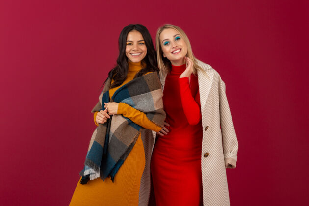 魅力两位笑容可掬的时尚女性穿着秋冬时装和外套 在红墙上孤零零地摆着姿势漂亮外套成人