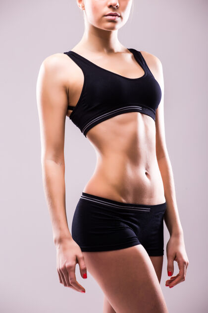 女性肌肉发达的年轻女运动员站在灰色的墙上 双手放在臀部往下看健身形状美容