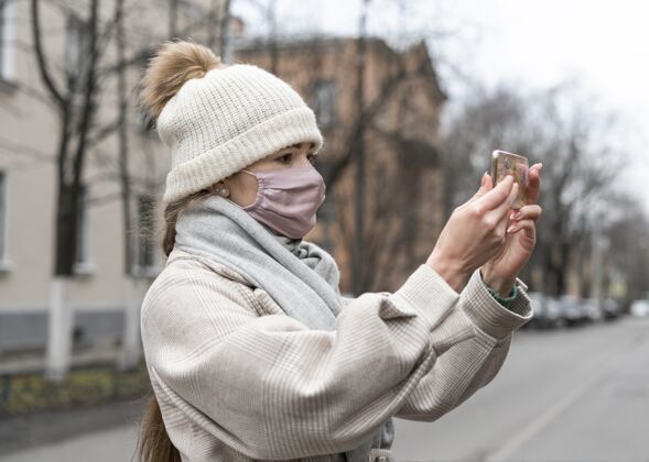 公民戴着医用面罩的女士在户外打视频电话的侧视图大流行女性预防措施
