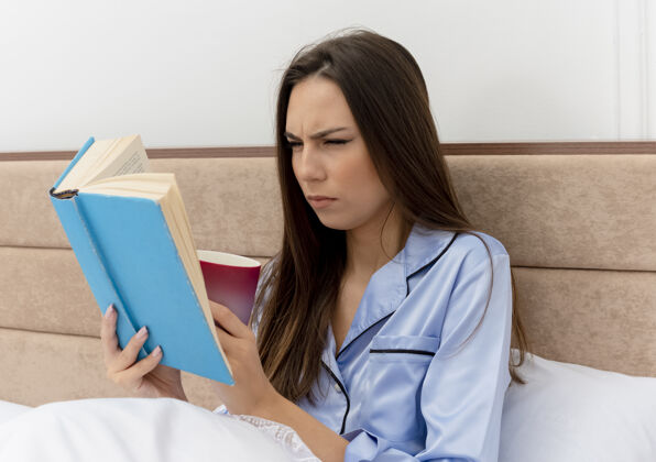 卧室穿着蓝色睡衣躺在床上的年轻漂亮女人严肃阅读女人