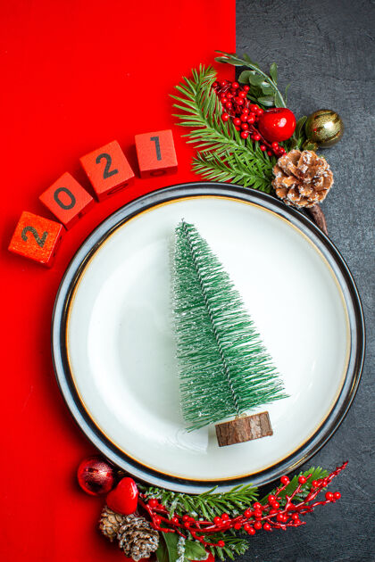 盘子新年背景的垂直视图与圣诞树晚餐盘装饰配件杉木枝和数字在一个黑色的桌子上的红色餐巾餐巾树枝圣诞