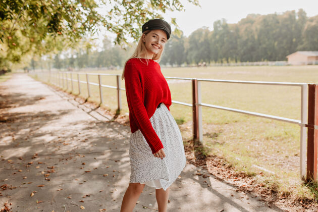 金发快乐的金发模特穿着红色休闲服看起来很时髦美丽的女人在公园的照片上露出欢快的微笑天气秋天户外