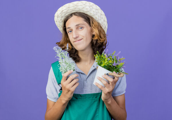 穿年轻的园丁 穿着连体衣 戴着帽子 手里拿着盆栽植物站锅男人