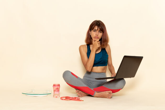 健康年轻女性穿着蓝色衬衫 身体健康 在浅白墙上使用笔记本电脑的前视图身体私人教练政权