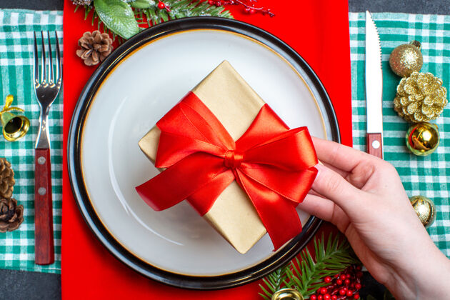视图顶视图手拿着一个漂亮的礼品盒与蝴蝶结形状的红丝带在一个盘子和餐具集装饰配件绿色剥离毛巾盘子餐具圣诞节