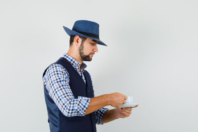 模特年轻人穿着衬衫 背心 戴着帽子喝着茶 看上去很小心眼镜年轻肖像