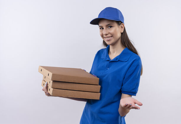 微笑身穿蓝色制服 头戴鸭舌帽的年轻送货女孩拿着一叠比萨饼盒看着镜头 开心地微笑着伸出手臂要求付款送货女孩欢呼