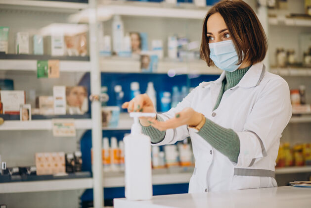 工作年轻的女药剂师用消毒剂洗手可维19化学家商店