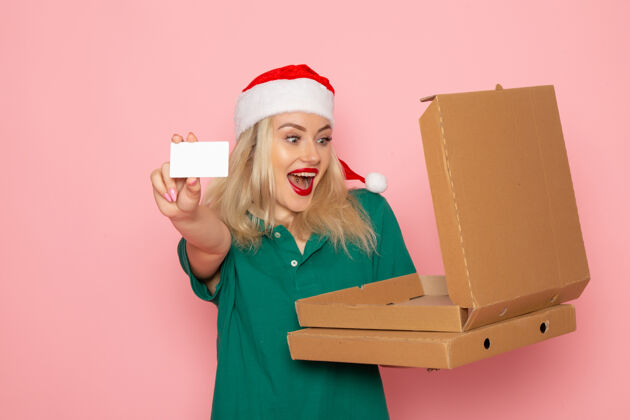 年轻女性正面图：年轻女性手持银行卡和披萨盒 粉色墙面 彩色节日圣诞照片 工作服制服工作颜色