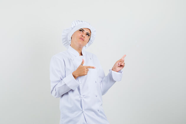 工作女厨师指着旁边和上面穿着白色制服 显得犹豫不决准备制服新鲜