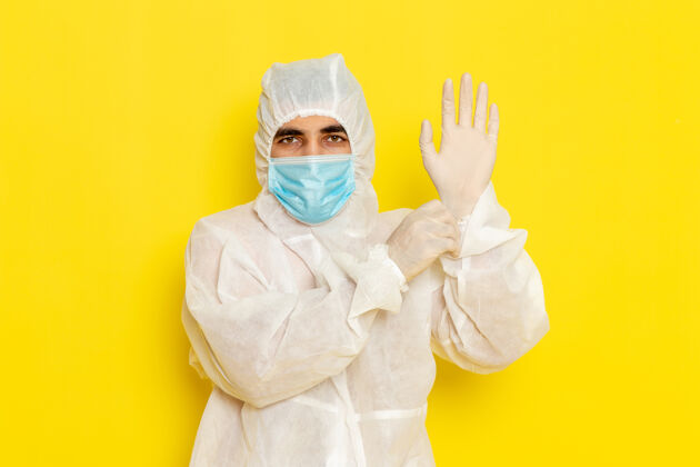 手套身穿特殊防护服 戴着面罩 戴着手套的男性科学工作者的正面图 浅黄色的墙上面罩科学穿戴