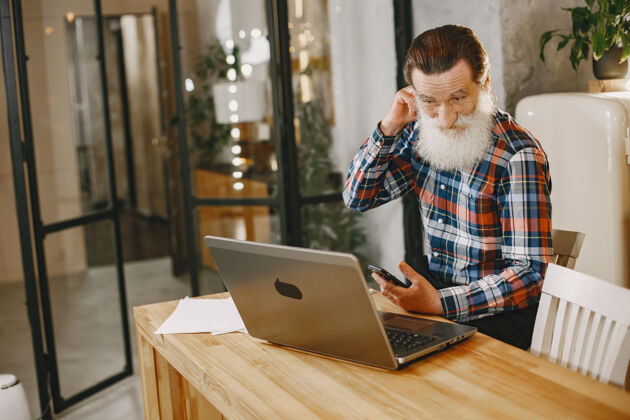 笔记本电脑老人拿着笔记本电脑爷爷坐在圣诞装饰品里老人拿着手机内容网站工作