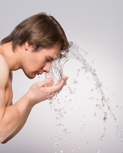 强一个英俊的男人在灰色的墙上用水洗脸的肖像轮廓成人肌肉