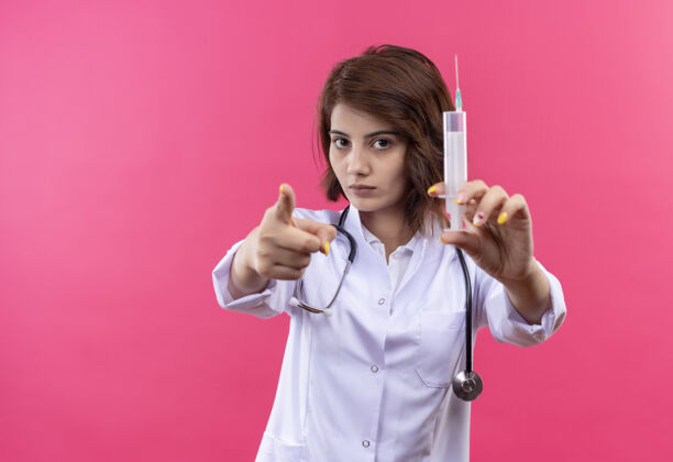 医生穿着白大褂的年轻女医生拿着听诊器拿着注射器用手指指着摄像机手指听诊器女士