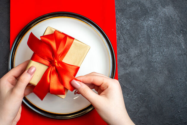 弓国家圣诞餐背景俯视图 黑色桌子上的红色餐巾上 手拿着空盘子 蝴蝶结形状的红丝带弓形空盘子国家