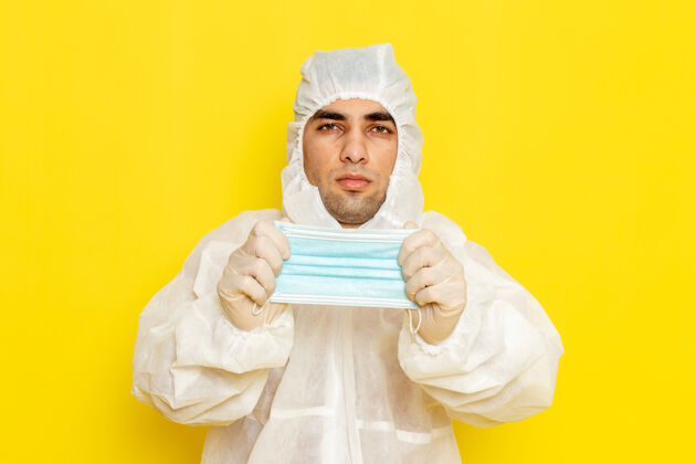 带身穿特殊防护服的男科学工作者在淡黄色墙上摘下面具的正面图服装男性淋浴帽