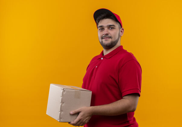 红色年轻的送货员穿着红色制服 戴着帽子 手里拿着盒子 微笑着自信帽子盒子制服