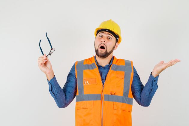建筑年轻的建筑工人穿着衬衫 背心 戴着头盔 戴着眼镜 看上去很困惑工作职业建筑