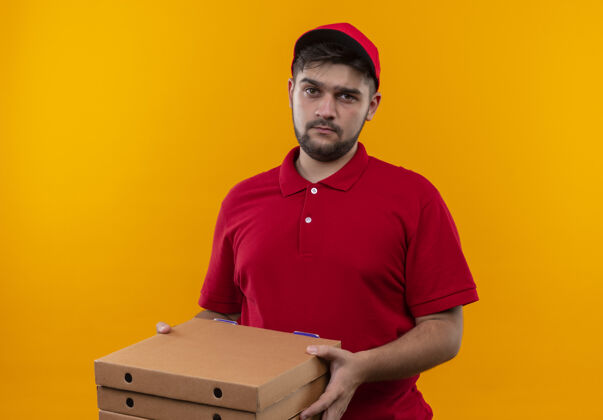 站着心烦意乱的年轻送货员穿着红色制服 戴着帽子 手里拿着一叠比萨饼盒 脸上带着悲伤的表情看着镜头堆着送货脸