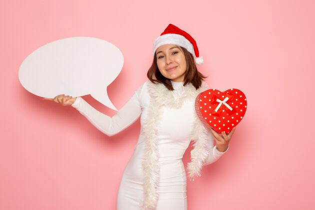 圣诞节正面图年轻女子手持白色大招牌 在粉色墙壁上献上雪花圣诞新年情感假期肖像服装情感