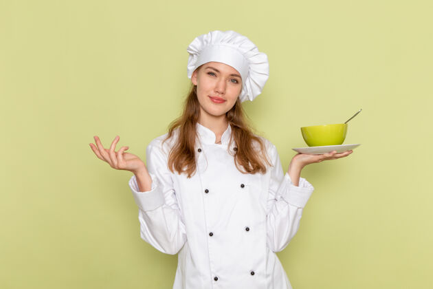 烹饪身着白色厨师服的女厨师正对着绿色的墙壁微笑着拿着绿色的盘子微笑头饰女厨师