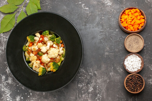 视图俯视图西兰花和花椰菜沙拉在黑碗不同的香料和削减胡萝卜碗在黑暗的表面香料碗炊具