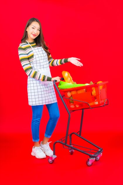 休闲在红色的隔离墙上 一位美丽的亚洲年轻女子拿着超市的购物篮购买商业篮子