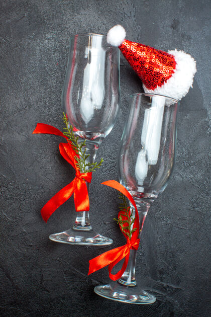 水瓶红色和黑色表面上的圣诞老人帽子玻璃高脚杯的垂直视图瓶子圣诞老人容器
