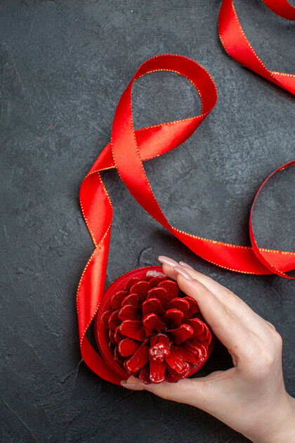 花手拿着黑色背景上的红丝带针叶树圆锥体的垂直视图浪漫玫瑰花瓣
