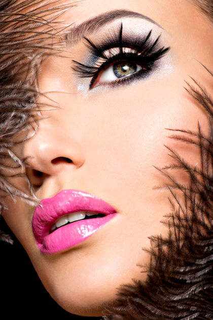 假美丽的女人用明亮的专业化妆品和羽毛靠近脸肖像阴影性感