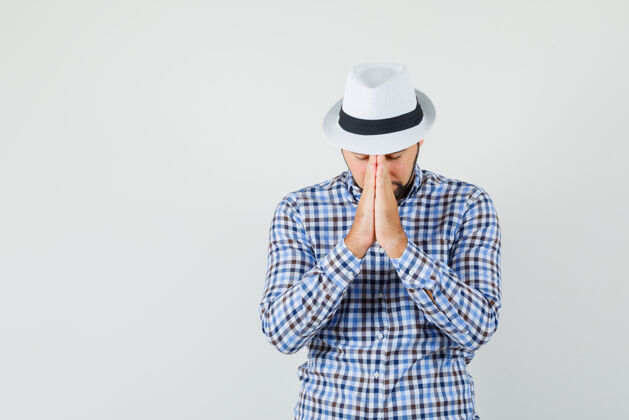 男人年轻人手牵手在祈祷的姿势在格子衬衫 帽子和看起来平静前视图帽子男性检查