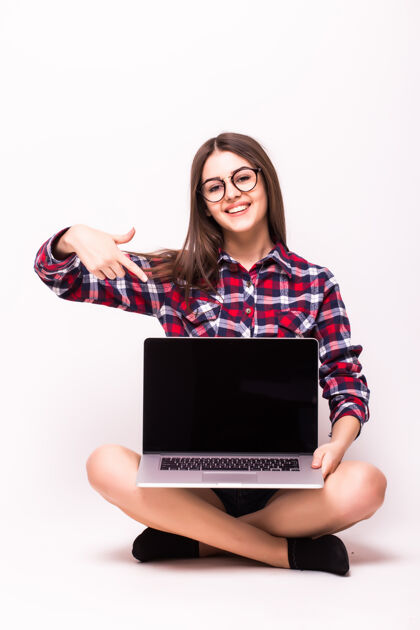 年轻一个坐在地板上的年轻女子指着屏幕 手里拿着一台白色笔记本电脑可爱互联网女性
