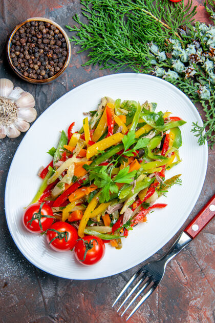 蔬菜沙拉俯瞰蔬菜沙拉在椭圆形盘子叉子大蒜黑胡椒在深红色的桌子上辣椒辣椒辣椒