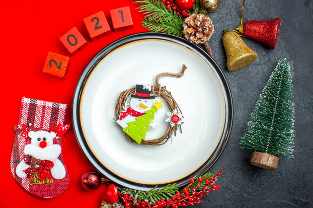 视图新年背景俯视图 餐盘上有红丝带装饰配件杉木树枝和数字圣诞袜放在黑色桌子上圣诞树旁的红色餐巾上树枝托盘头顶