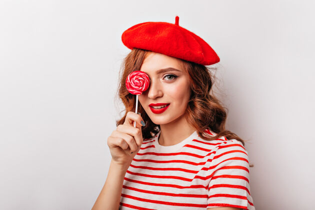 表情欣喜若狂的红发女孩拿着糖果站在那里优雅的法国女人拿着棒棒糖的室内肖像Swoosh姜棒棒糖