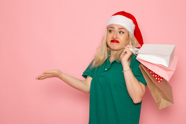 包装正面图年轻女性拿着圣诞礼物在粉红色的墙壁上包模型假日圣诞节新年照片的颜色风景年轻女性肖像
