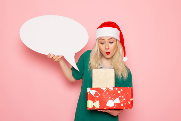 女人正面图年轻女性手持圣诞礼物和白色标志在粉色墙上的女性礼物彩色照片新年假期颜色圣诞节风景