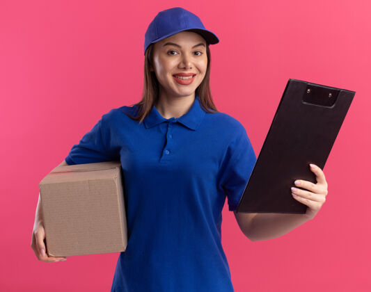 女人穿着制服的微笑漂亮的送货员拿着卡片盒和剪贴板 隔离在粉红色的墙上 还有复印空间漂亮微笑送货
