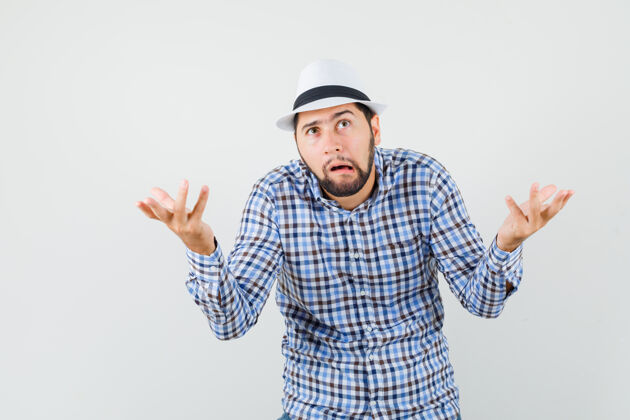 男性一个穿着格子衬衫 戴着帽子 满脸困惑的年轻人做着无助的手势休闲发型帽子