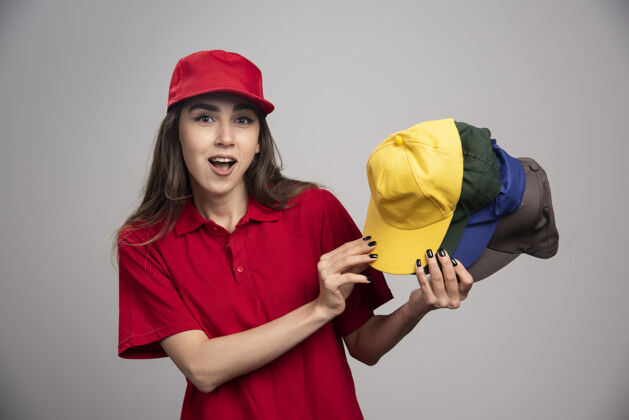 帽子戴着彩色帽子的送货员在灰色的墙上摆姿势帽子制服雇员