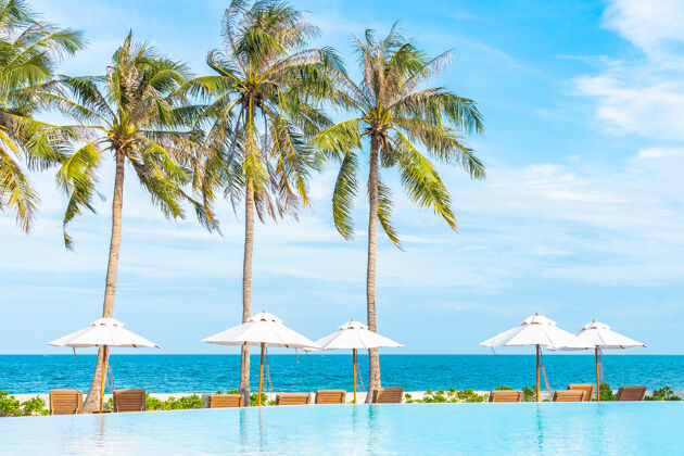 岛屿酒店度假区的户外游泳池周围有雨伞和躺椅 有海边沙滩和椰子树景观天空别墅