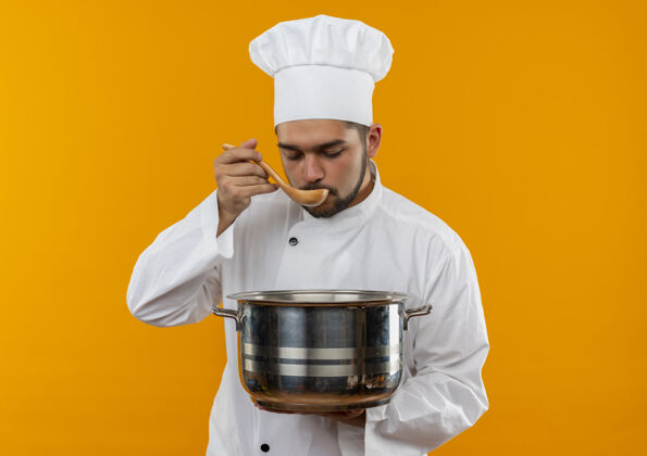 橙色年轻的男厨师穿着厨师制服拿着锅 用勺子吃着孤立的橘子空间锅吃年轻