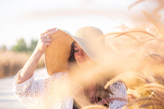 阳光美丽的年轻女子戴着一顶大帽子在田野的草丛写摆姿势波西米亚年轻